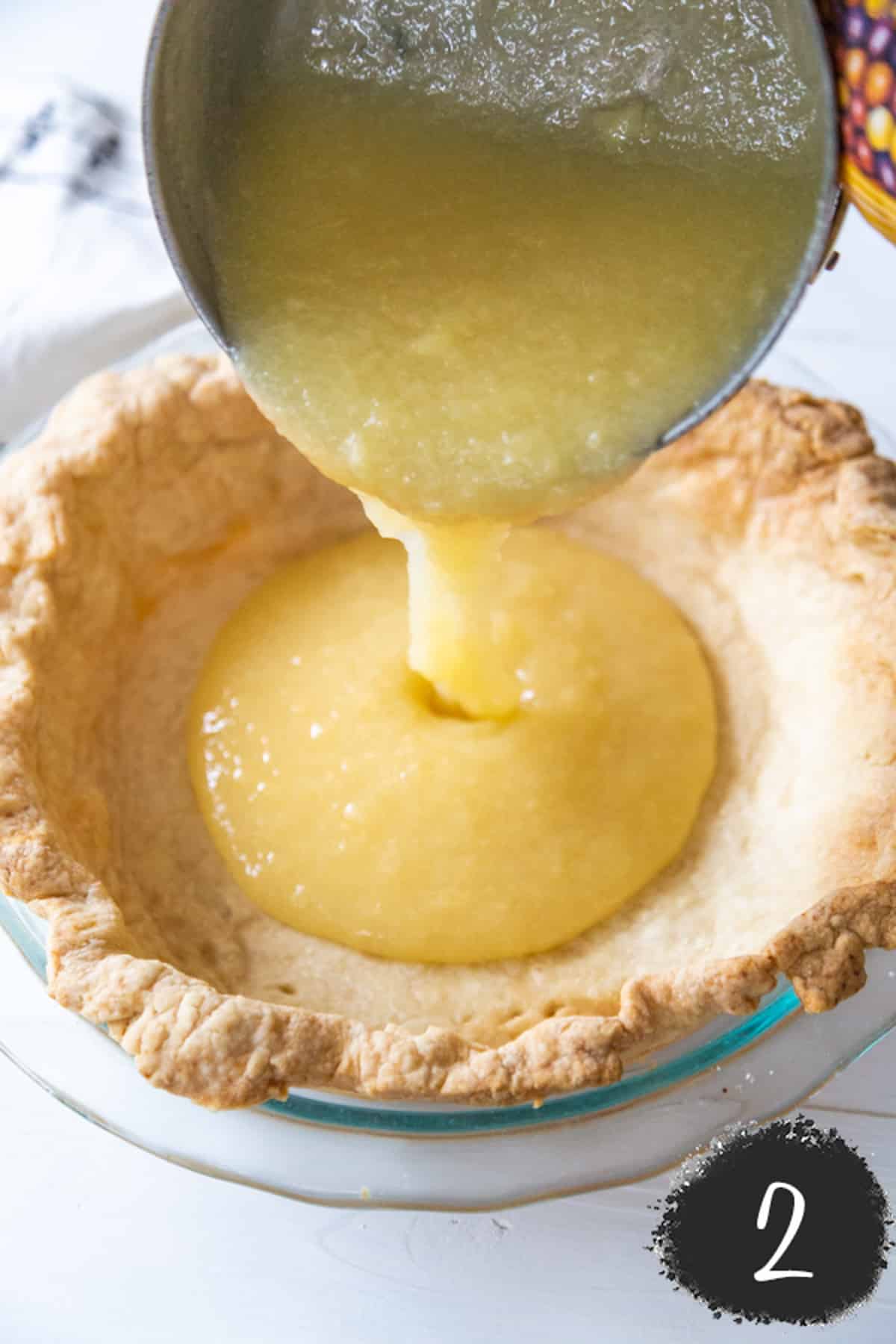 Lemon curd being poured into a baked pie crust.
