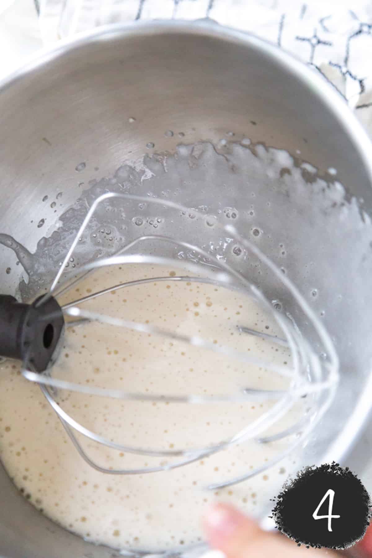 A silver mixing bowl filled with aquafaba and sugar, and a wire wisk.