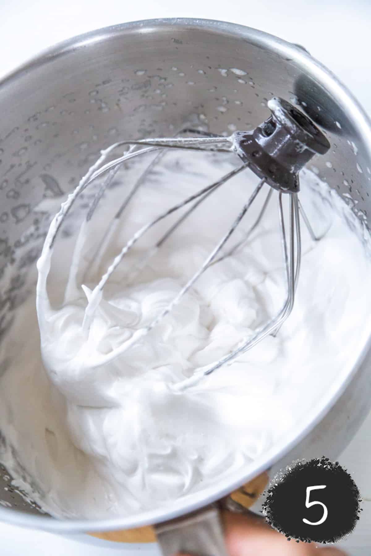Aquafaba meringue in a silver mixing bowl with a whisk.