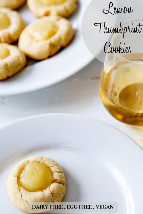A PInterest pin for vegan lemon thumbprint cookies with a picture of a cookie on a white plate and a plate full of cookies and a glass of wine next to it.