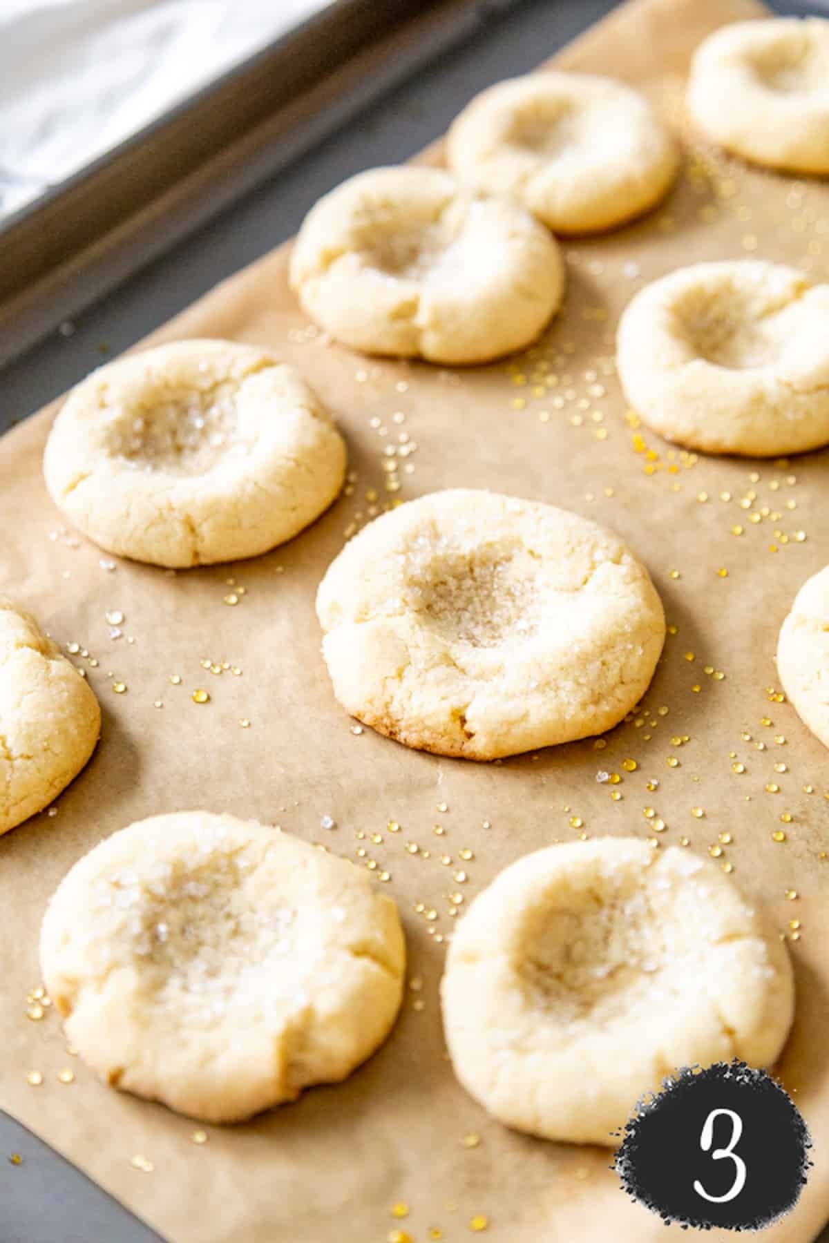 A cookie sheet with unbaked sugar cookies with indentations in the center of the cookies.