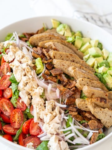 A Cobb salad with vegan chicken and bacon bits in a large white bowl.