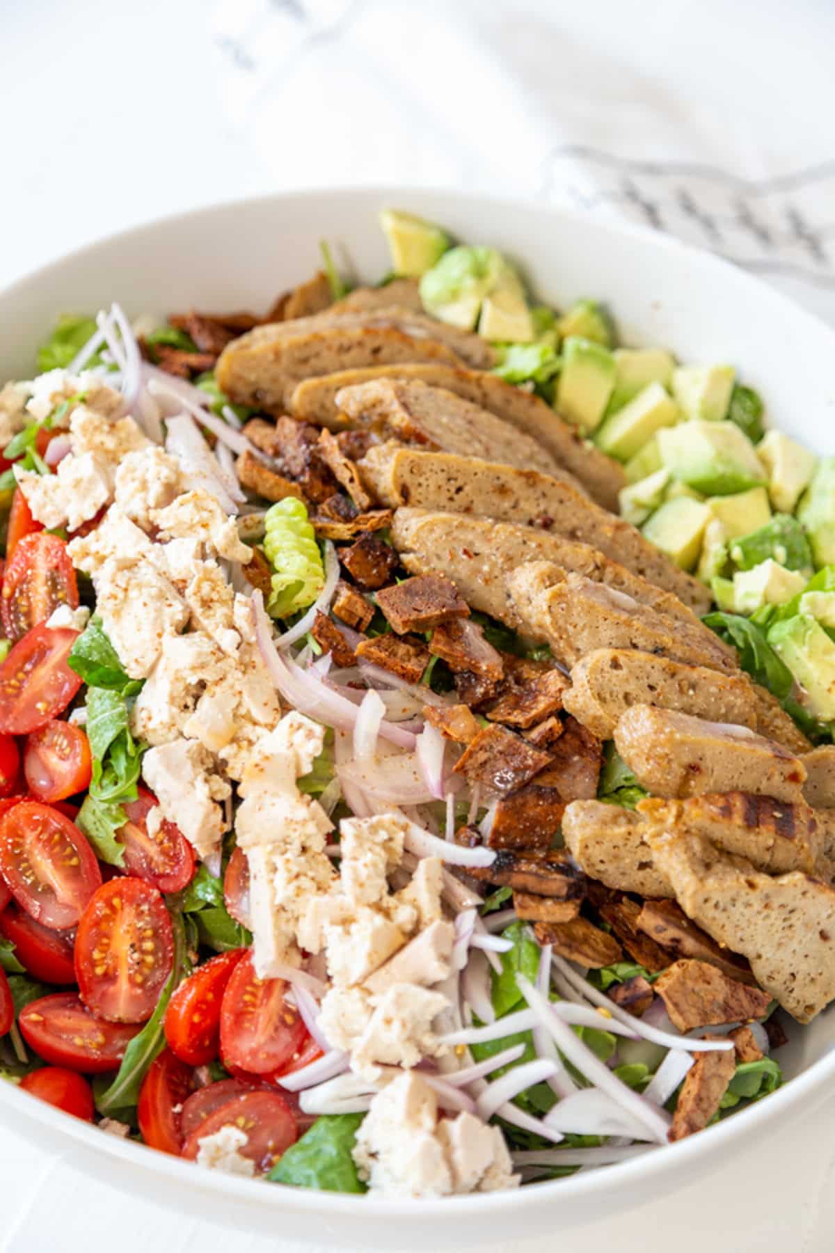 A Cobb salad with vegan chicken and bacon bits in a large white bowl.