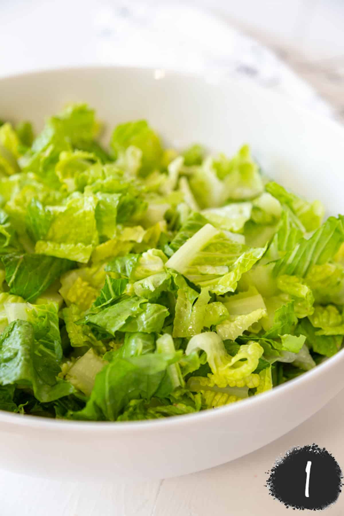 A white salad bowl filled with chopped lettuce.