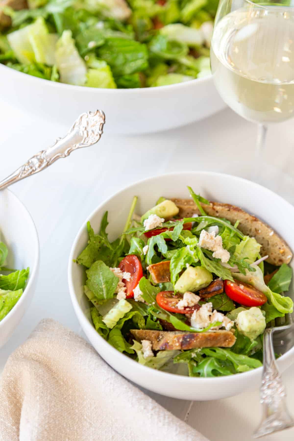 Vegan cobb salad in a white bowl with a silver spoon next to a glass of white wine.