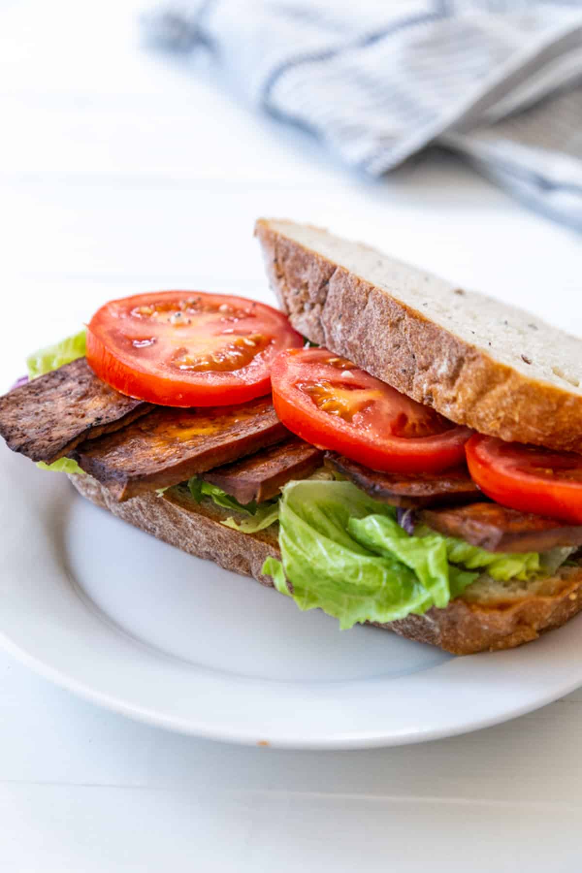A tofu bacon, lettuce, and tomato sandwich on a white plate.