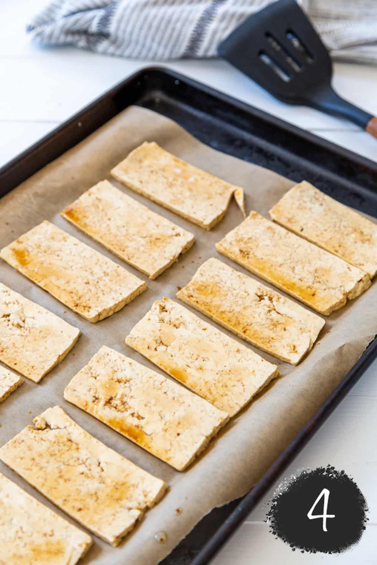 Thinly sliced tofu soaked in soy sauce on a parchment lined baking sheet.