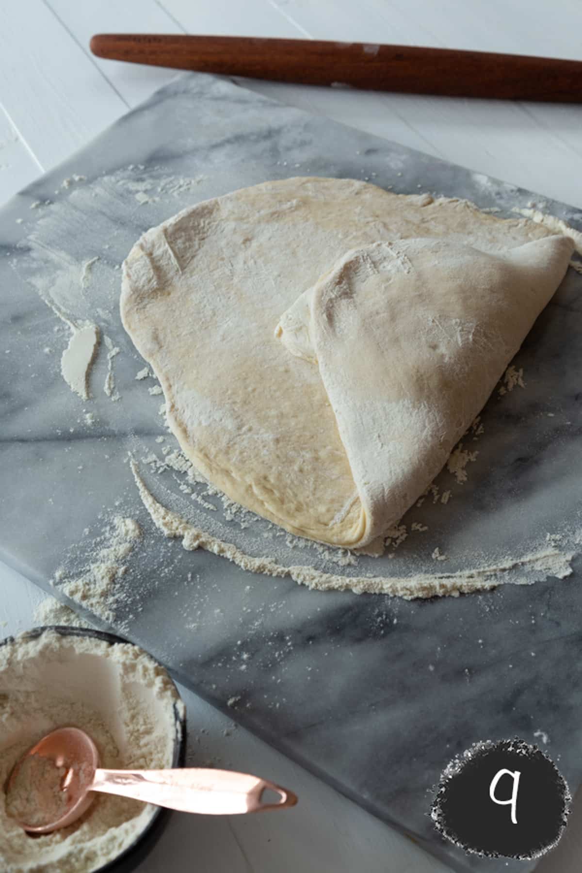 Rolled out croissant dough with a block of butter in the center and one segment of the dough folded over the butter.