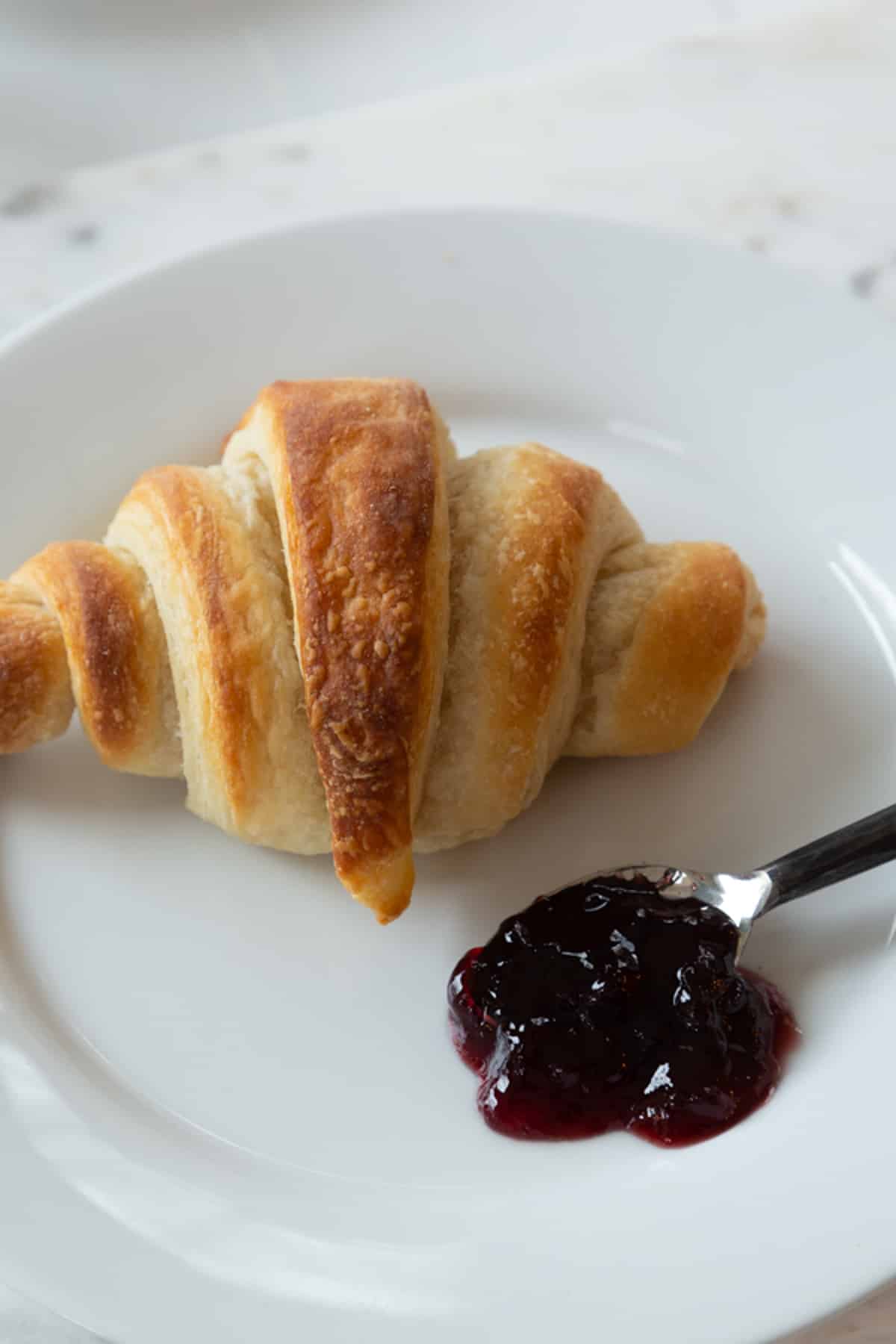 A croissant on a white plate with a spoon of preserves.