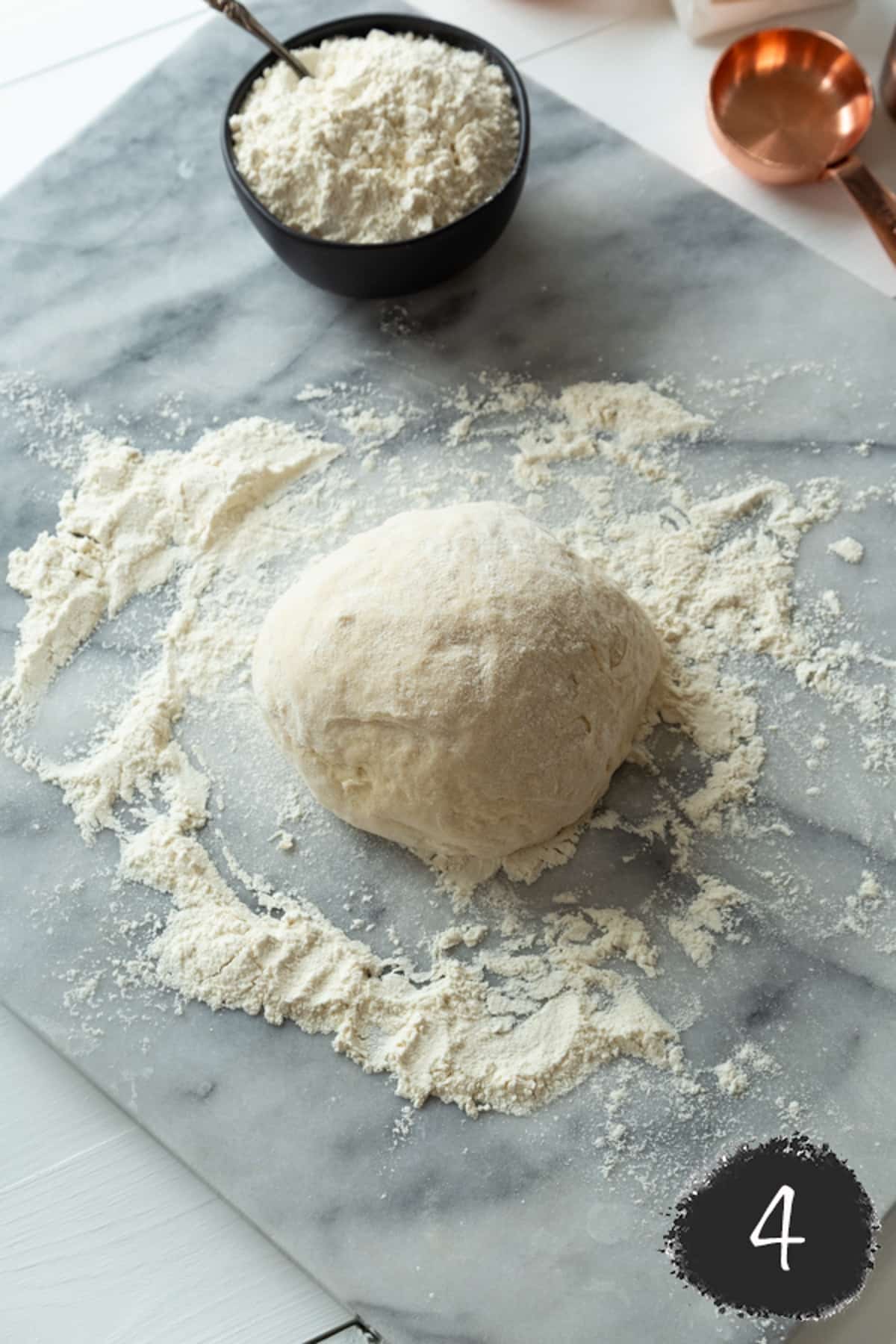 A ball of dough with flour on a marble surface.