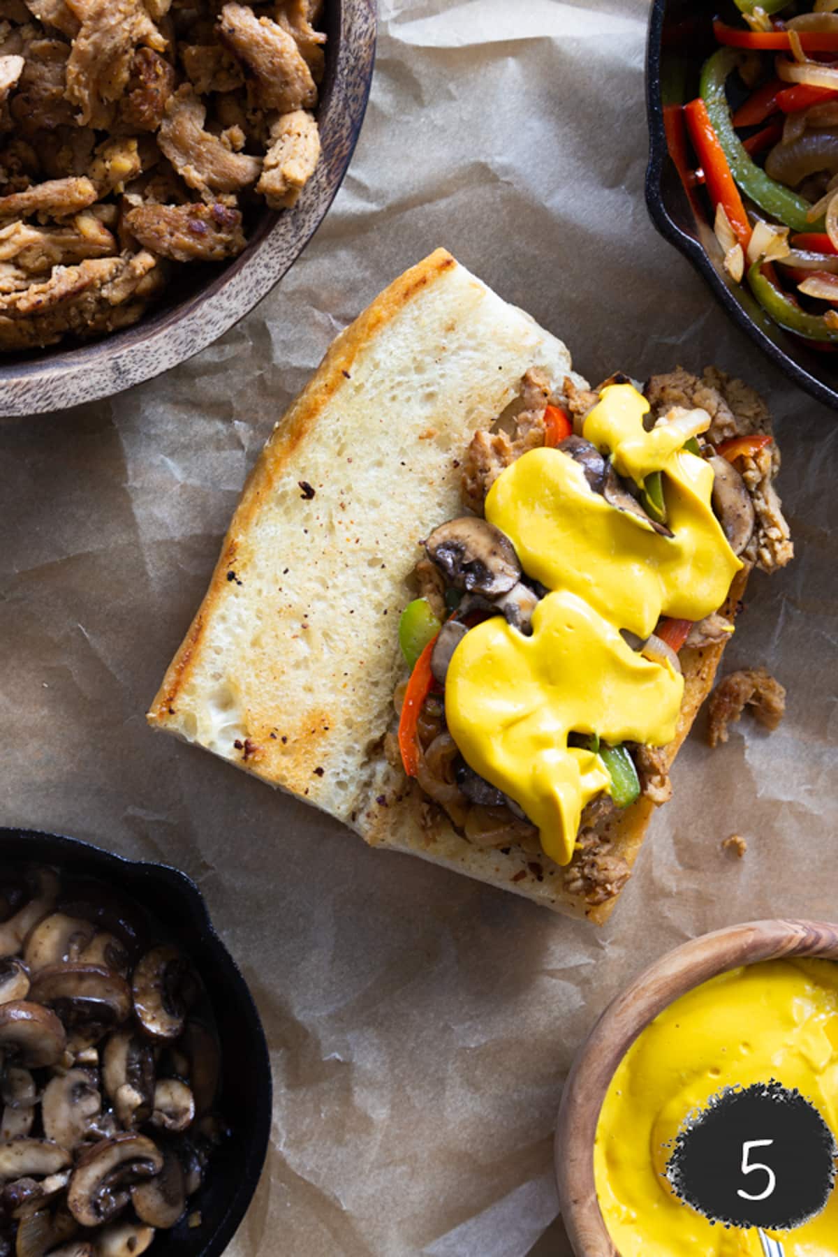 A vegan cheesesteak sandwich with the ingredients in bowls.