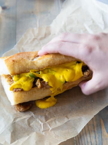 A hand holding a sandwich with cheese sauce.