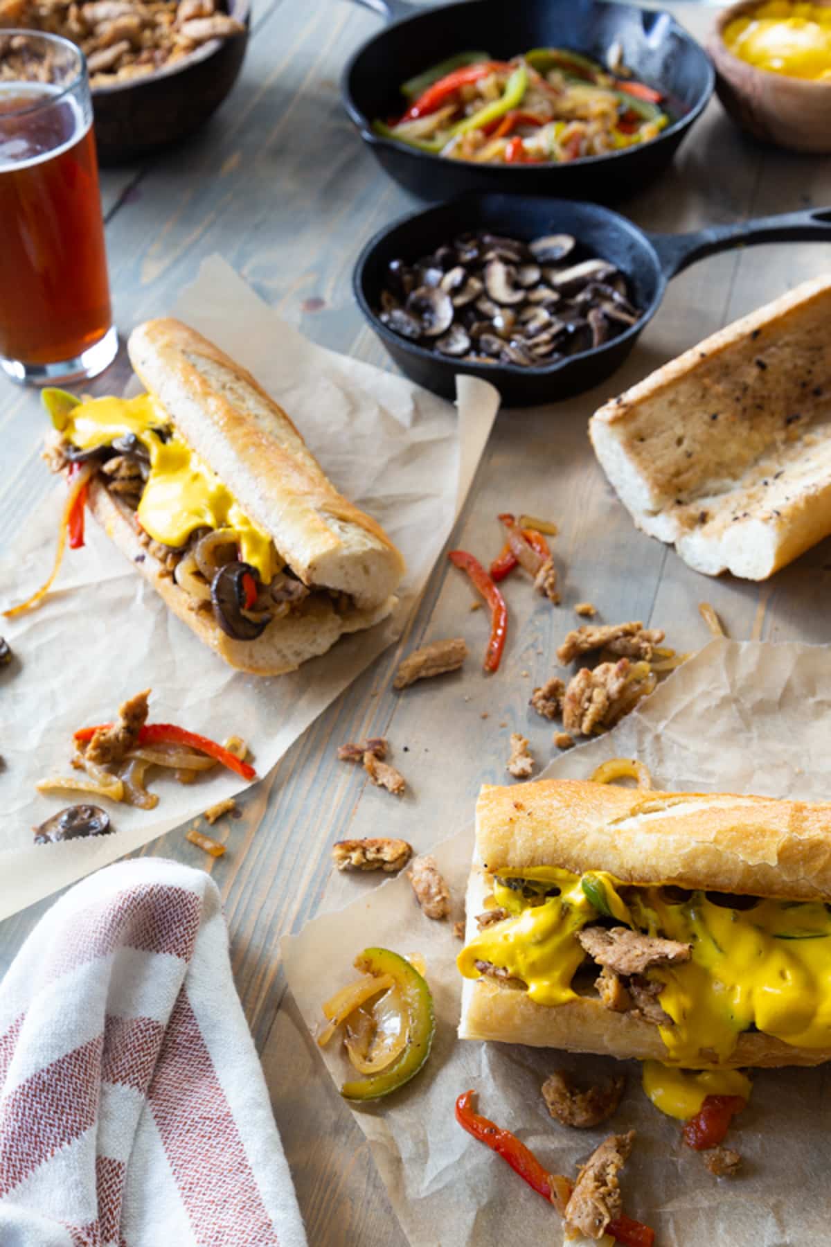 Vegan Philly cheesesteak sandwiches and pans of mushrooms and peppers.