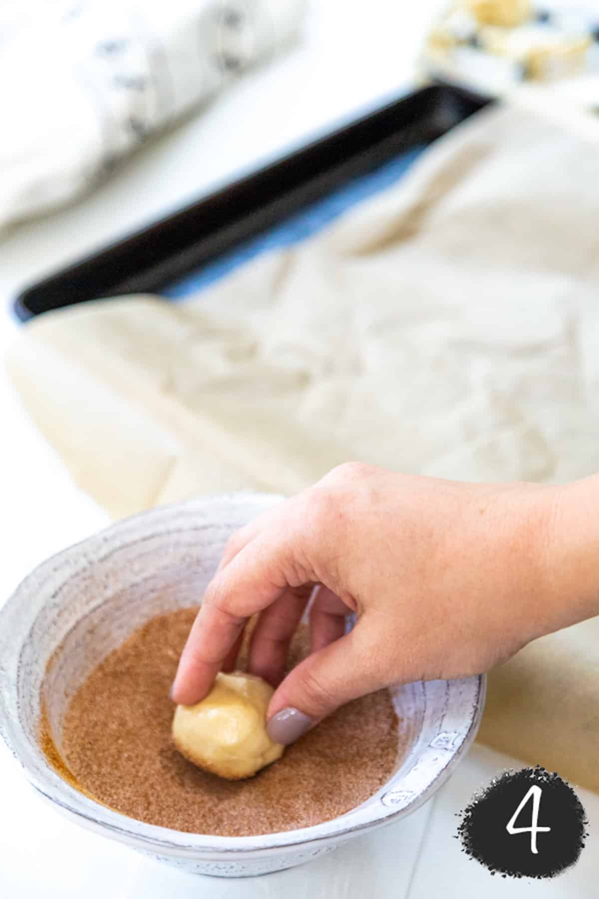 A hand rolling a ball of cookie dough in cinnamon sugar.