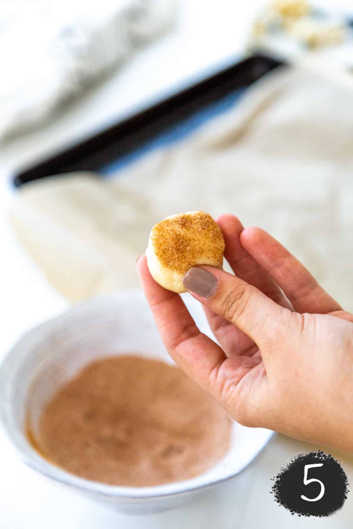 A hand holding a cookie dough ball covered in cinnamon sugar.