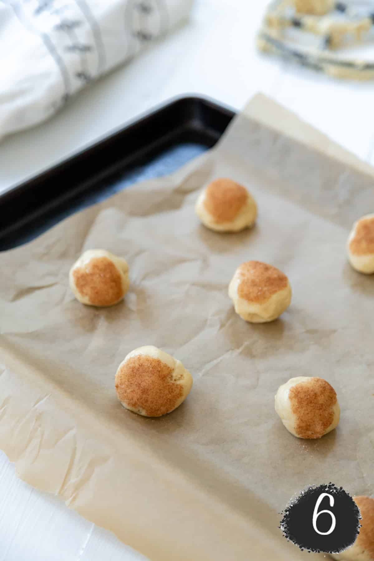 Snickerdoodle cookie dough balls on a parchment lined baking sheet.