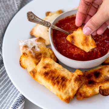 A hand dipping a pizza roll into a bowl of marinara sauce.
