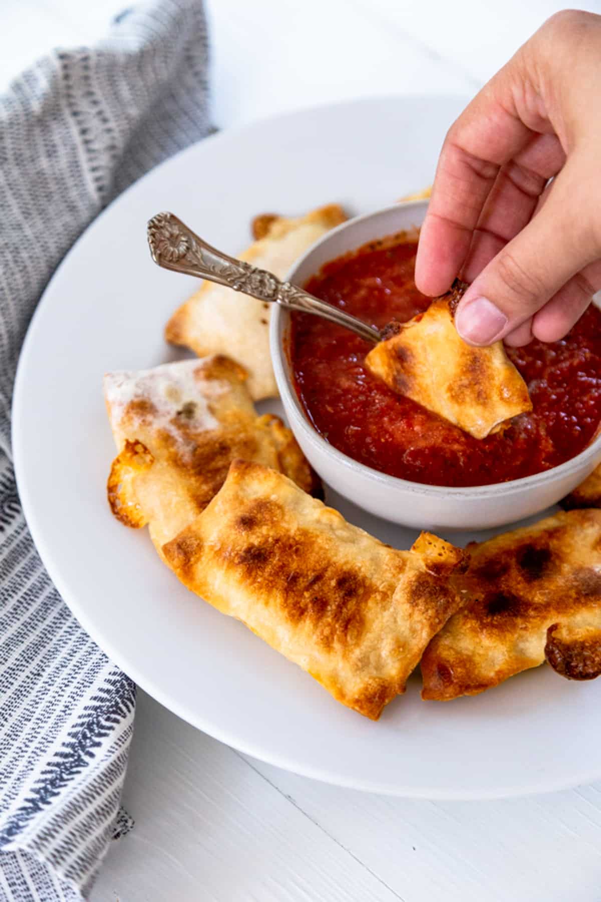 A hand dipping a pizza roll into a bowl of marinara sauce.