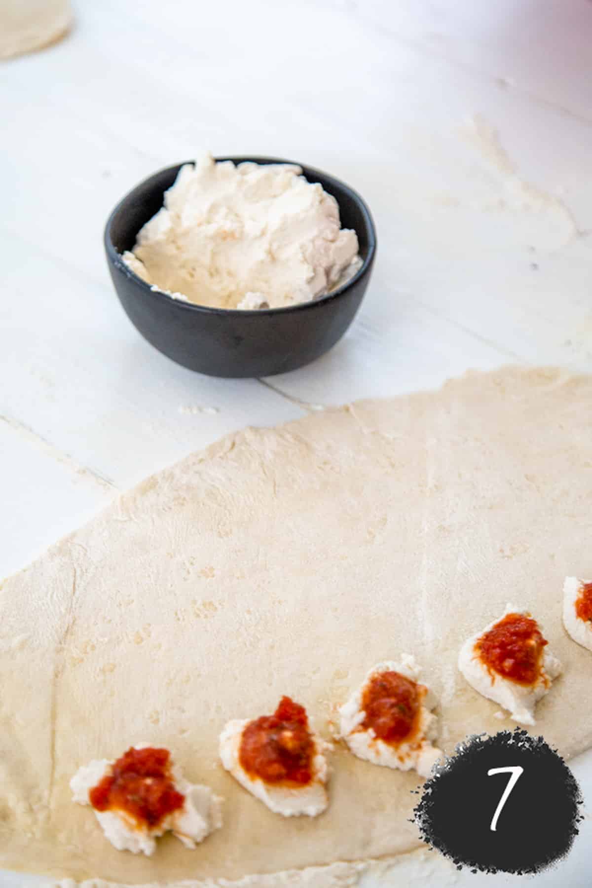 Rolled out pizza dough with ricotta cheese and pizza sauce.