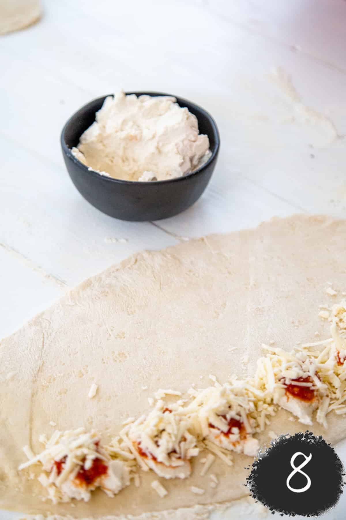 Cheese and sauce on rolled out pizza dough to make vegan pizza rolls.