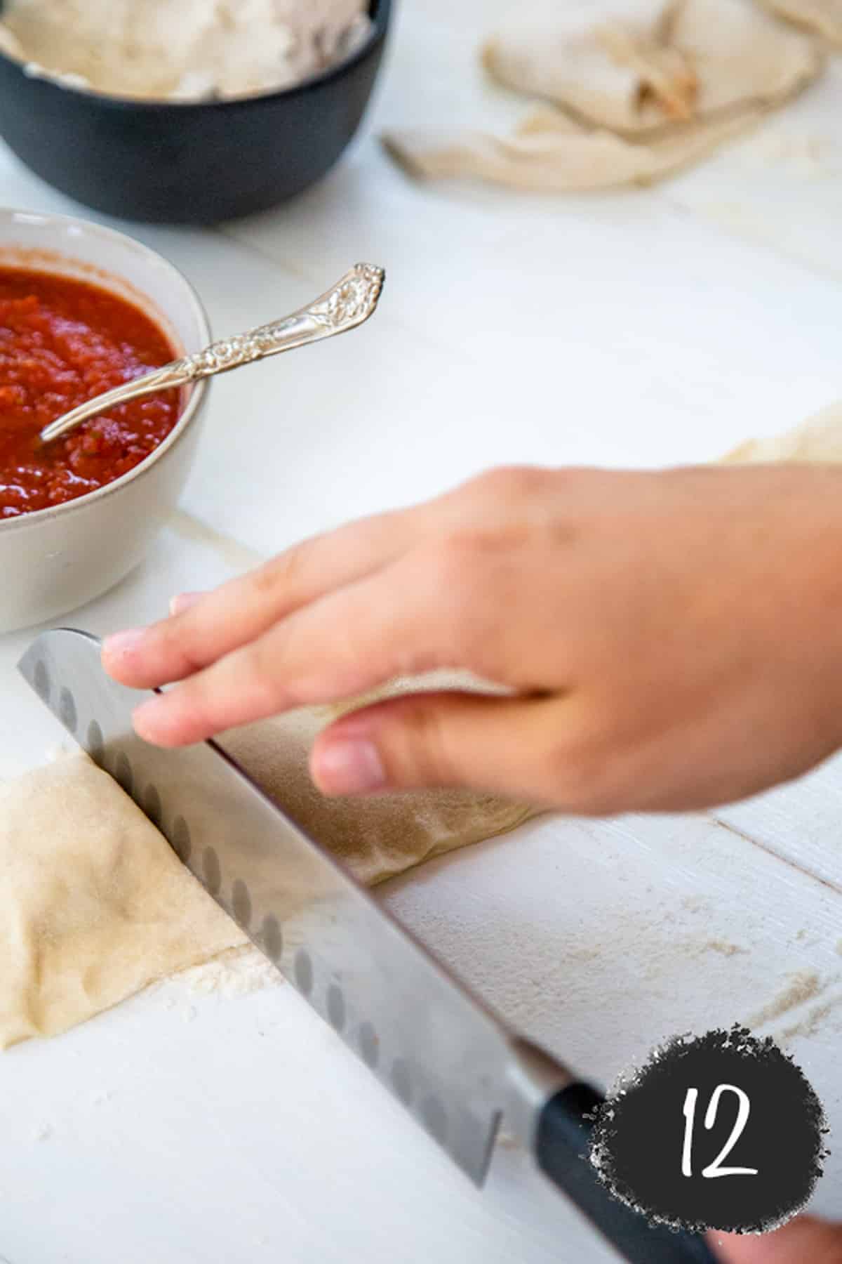 A hand cutting unbaked pizza rolls.