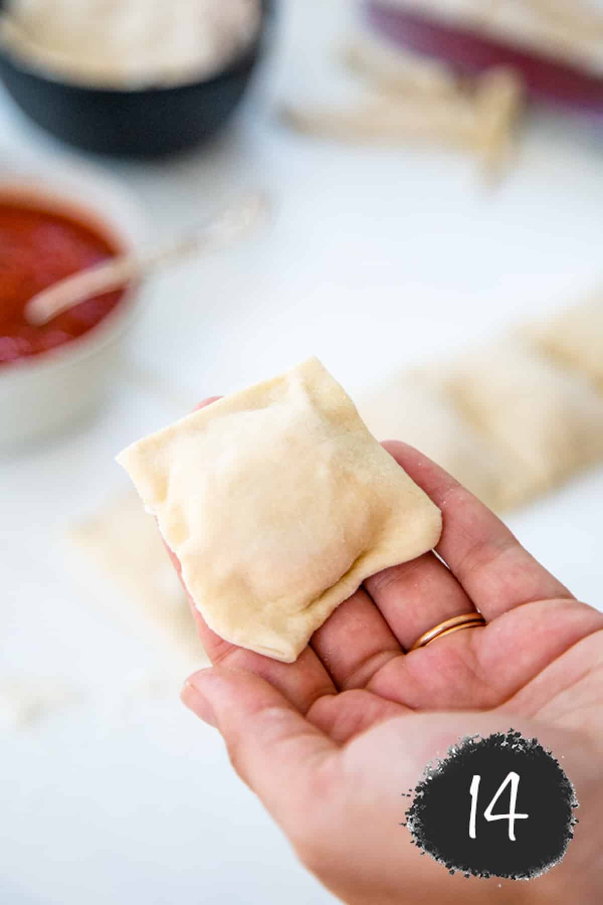 A hand holding an unbaked pizza roll.