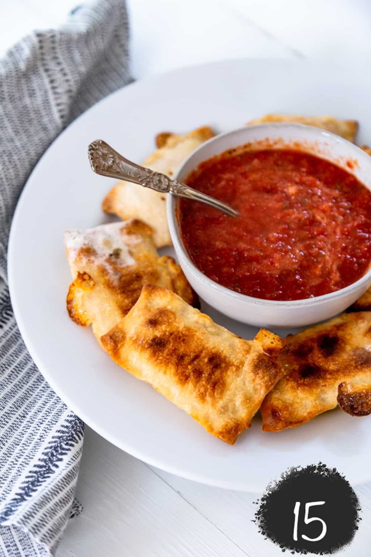 A white plate with pizza rolls and a bowl of marinara sauce.