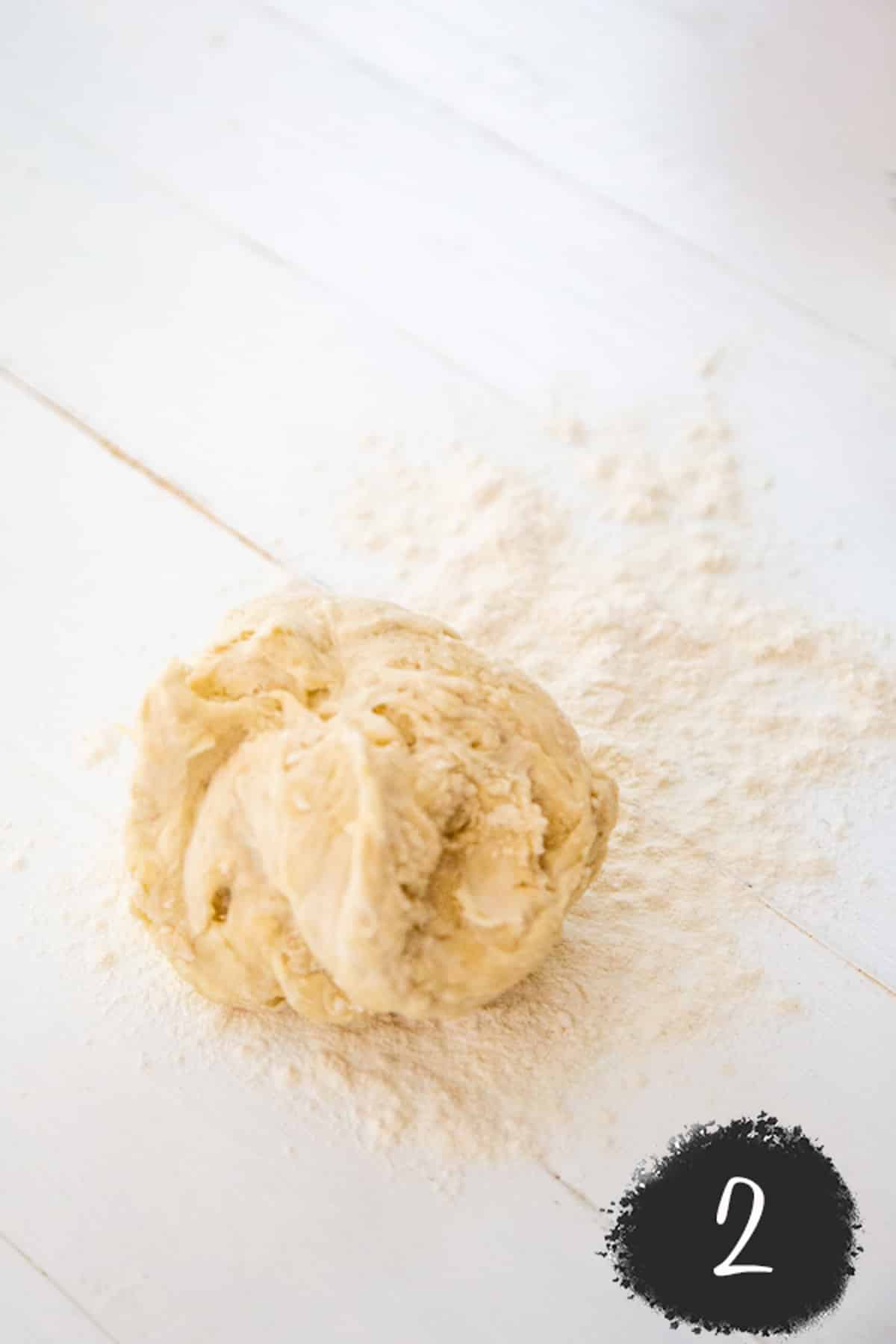 A ball of pizza dough on a white wood surface.