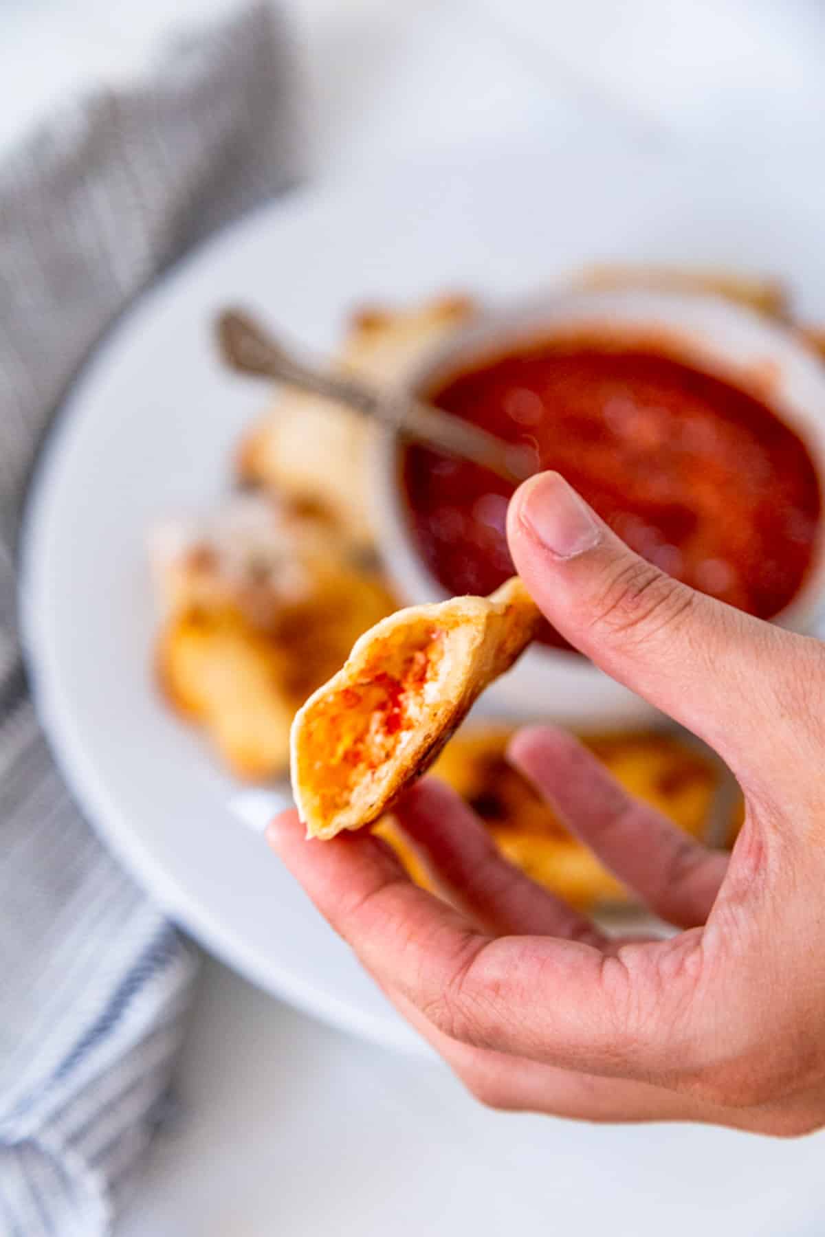 A hand holding a pizza roll with the filling showing.