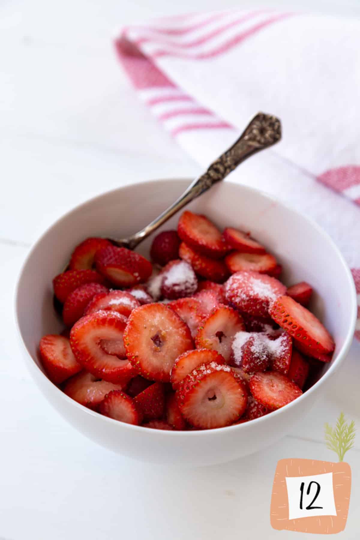 A white bowl with sliced strawberries macerating in sugar.