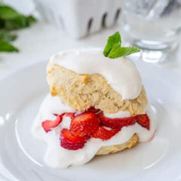 Vegan strawberry shortcake on a white plate with a white container filled with strawberries.