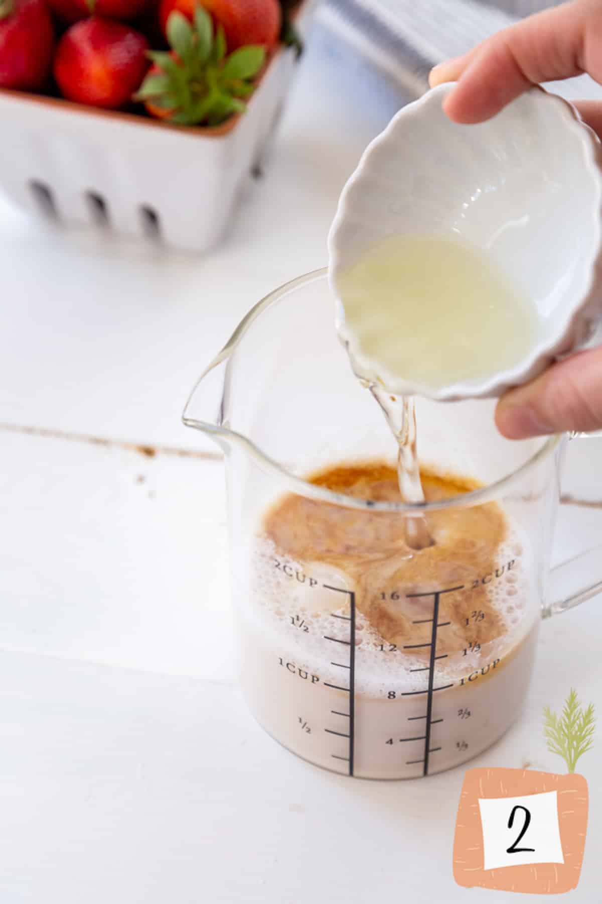 A hand pouring oil into a measuring cup of milk and cinnamon.