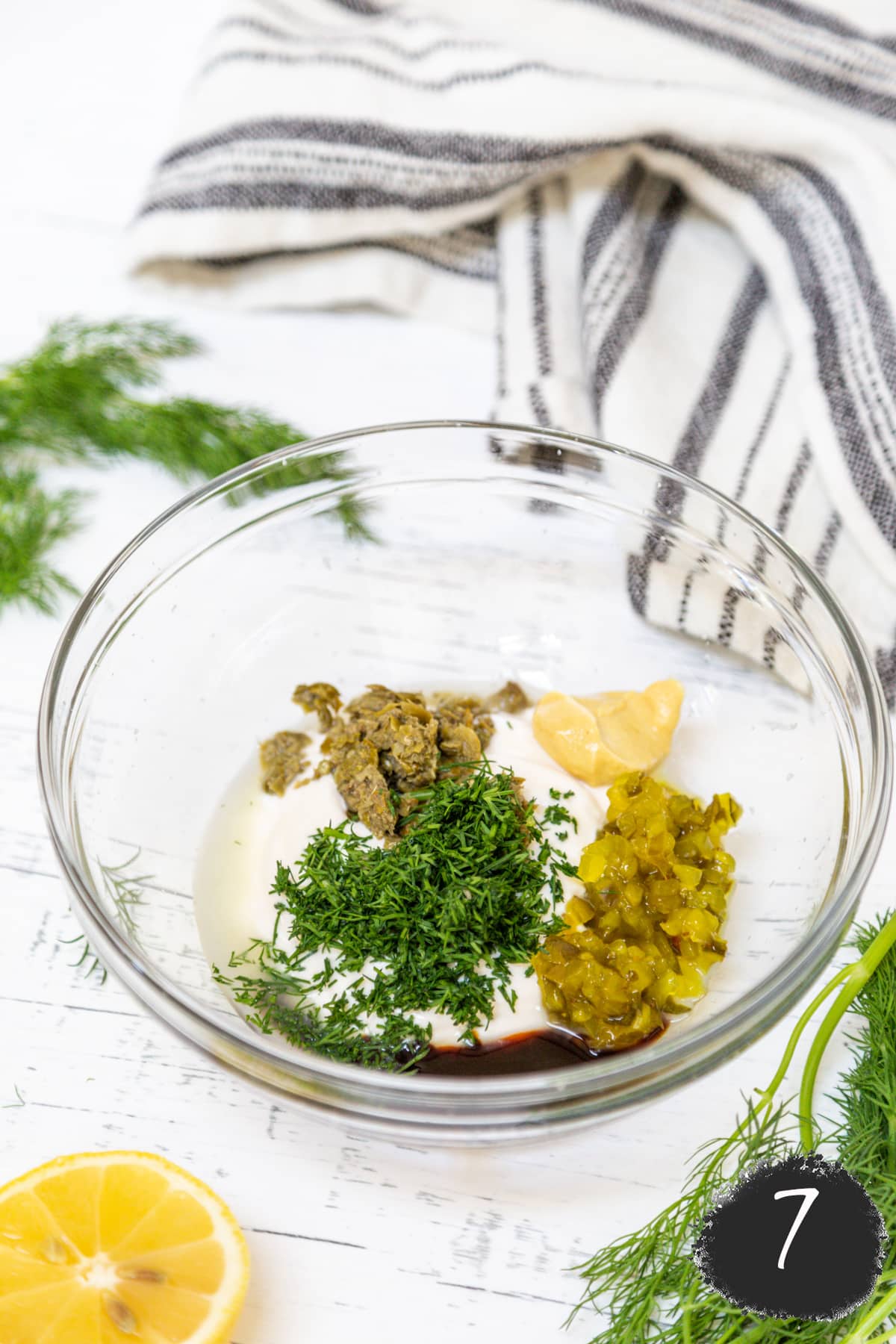 A glass mixing bowl with ingredients for vegan tartar sauce.