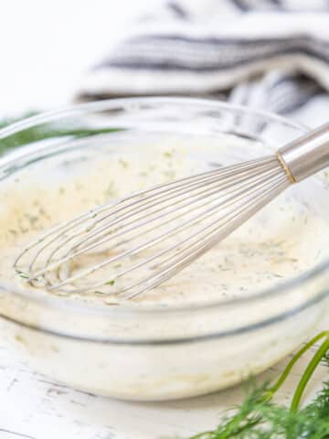A clear glass bowl of tartar sauce with a whisk.