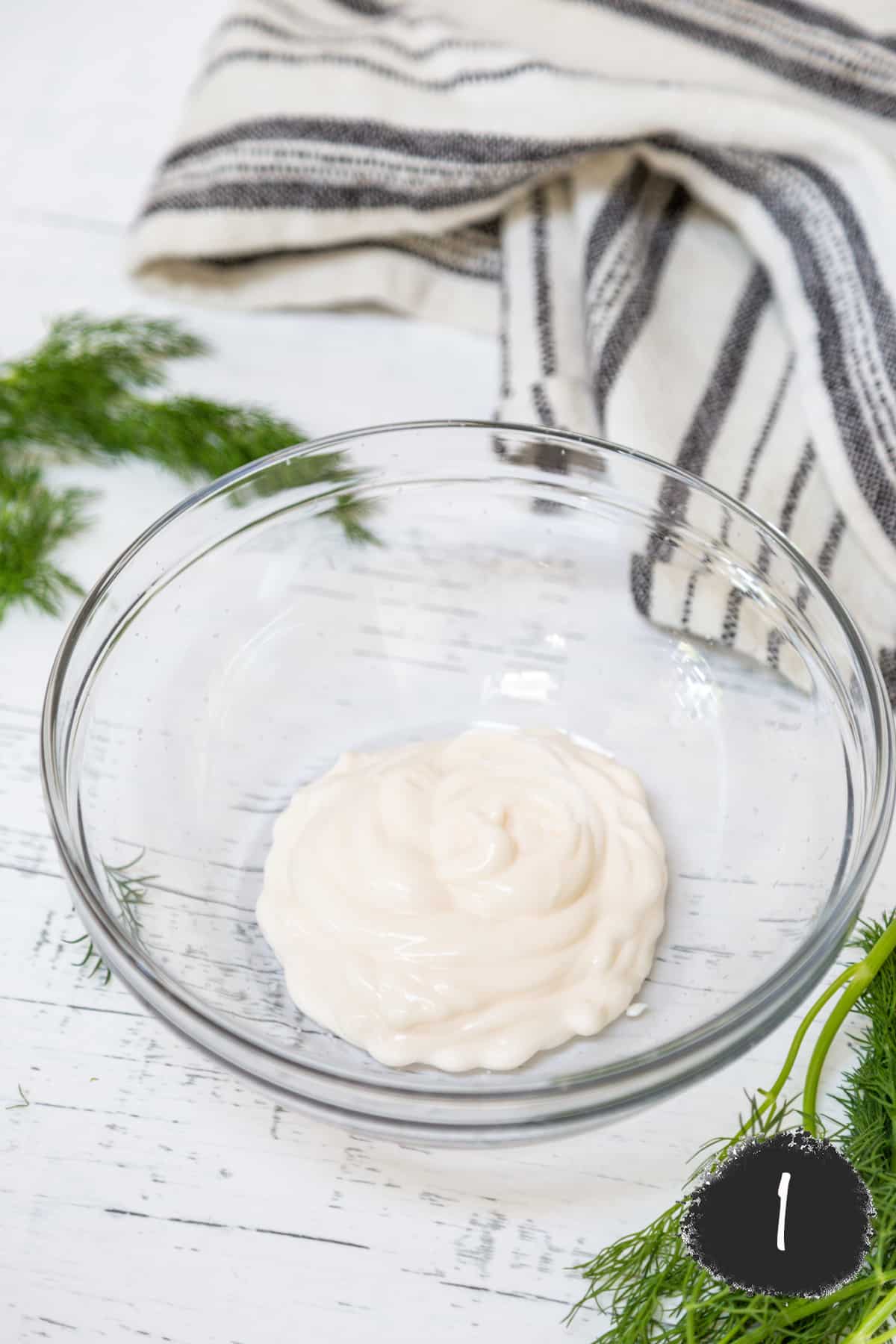 A glass bowl with mayo and dill on the side.