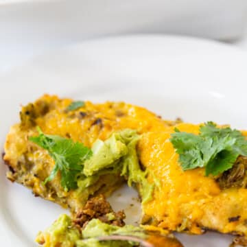 A fork cutting into an enchilada on a white plate.