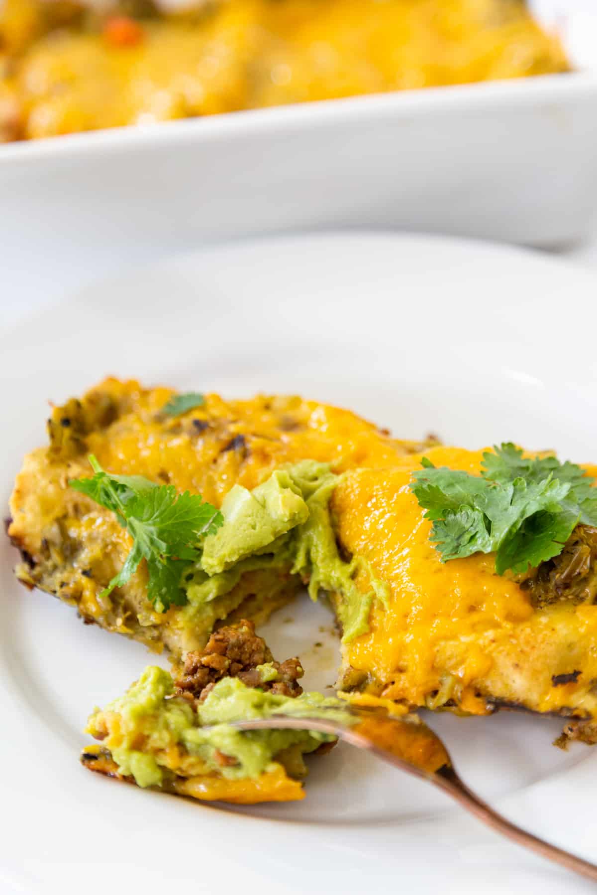 A fork cutting into an enchilada on a white plate.