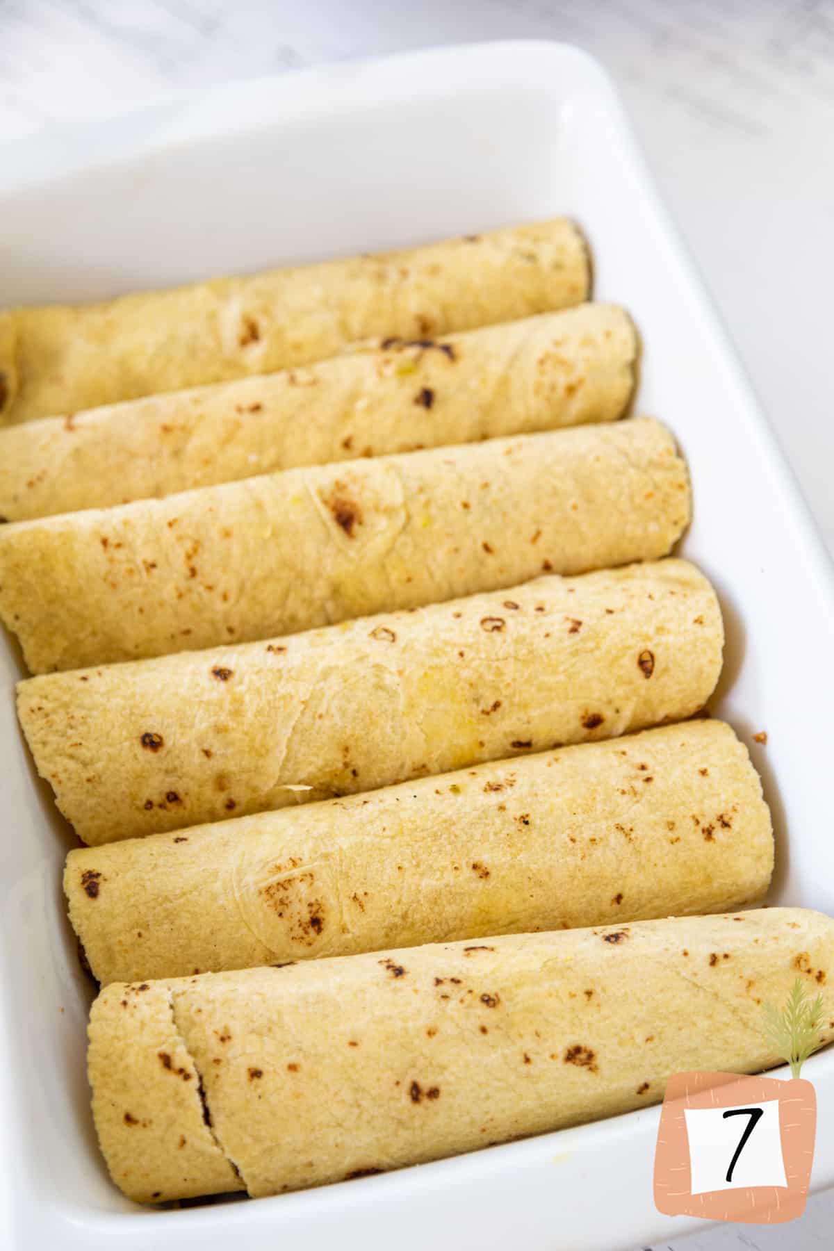 A white baking dish with rolled up corn tortillas.