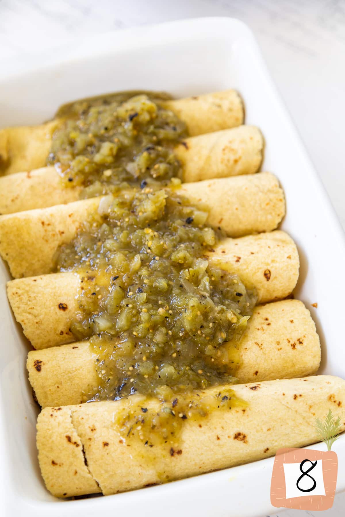 Rolled up corn tortillas with green salsa poured over the top.