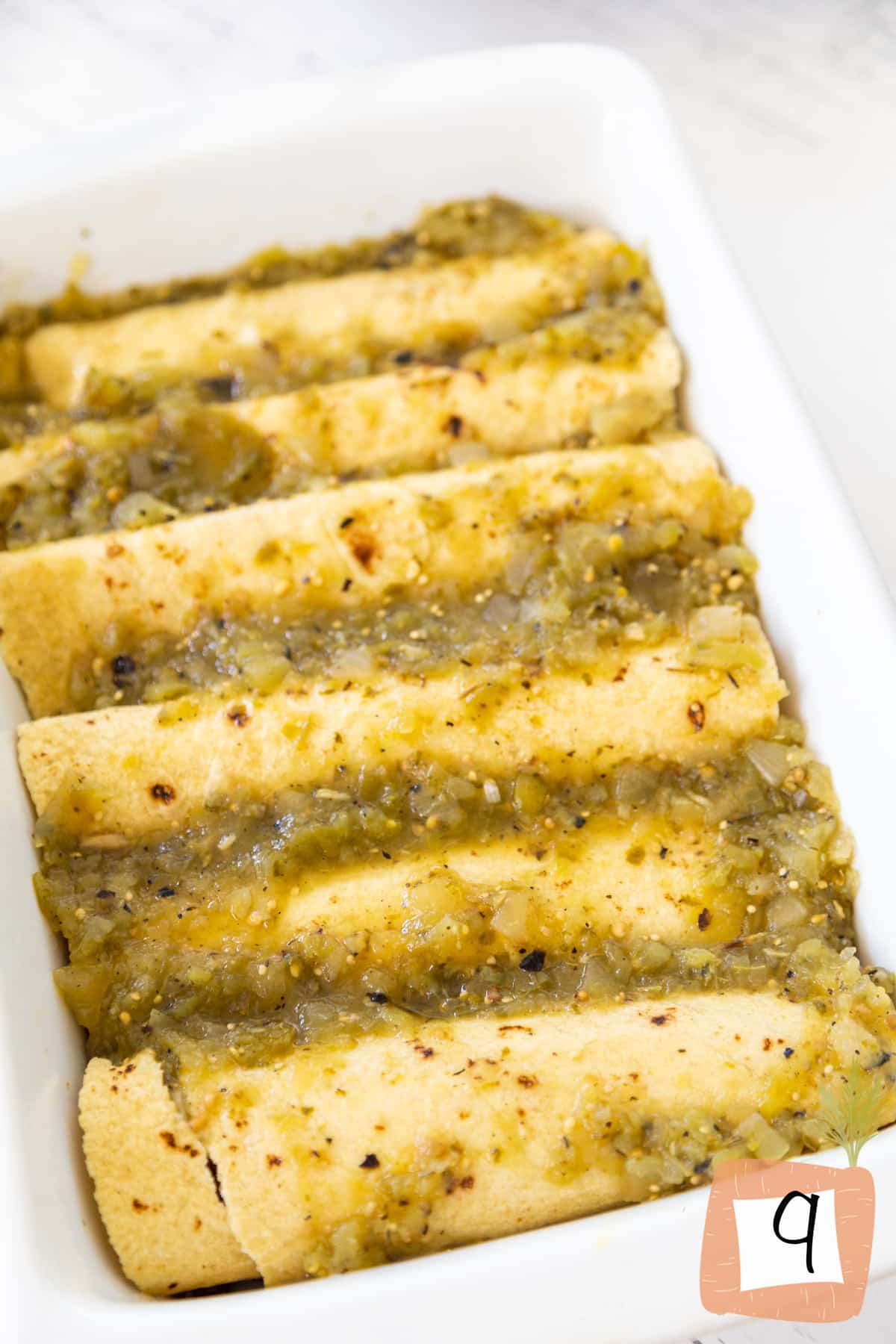 Rolled up corn tortillas covered in green salsa in a white dish.