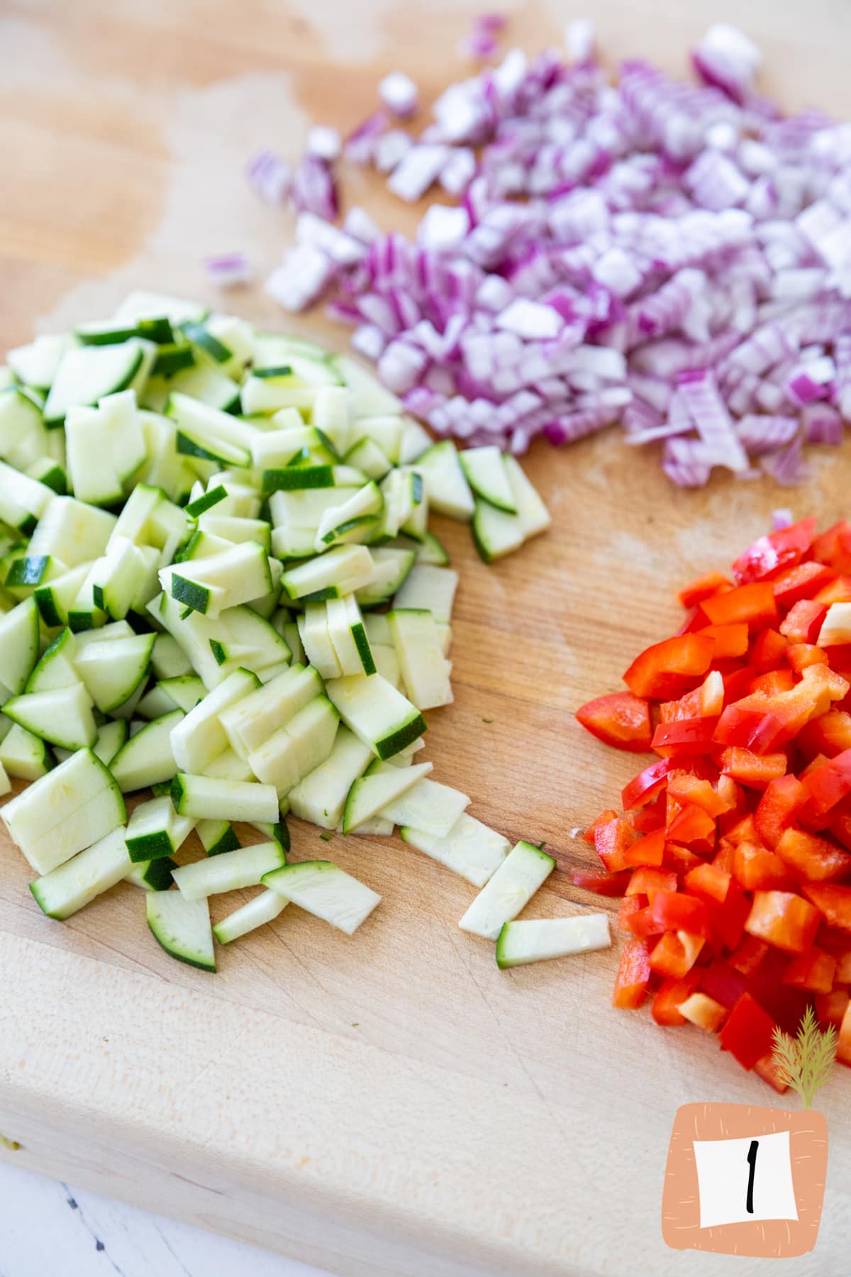 A wooden cutting board with diced red bell pepper, red onion, and zucchini.