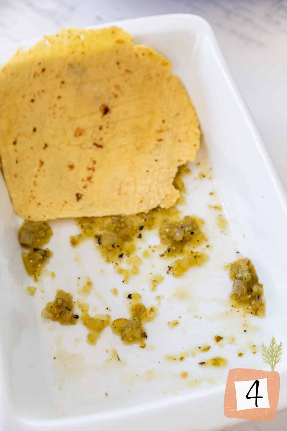 A white baking dish with green salsa and a corn tortilla.
