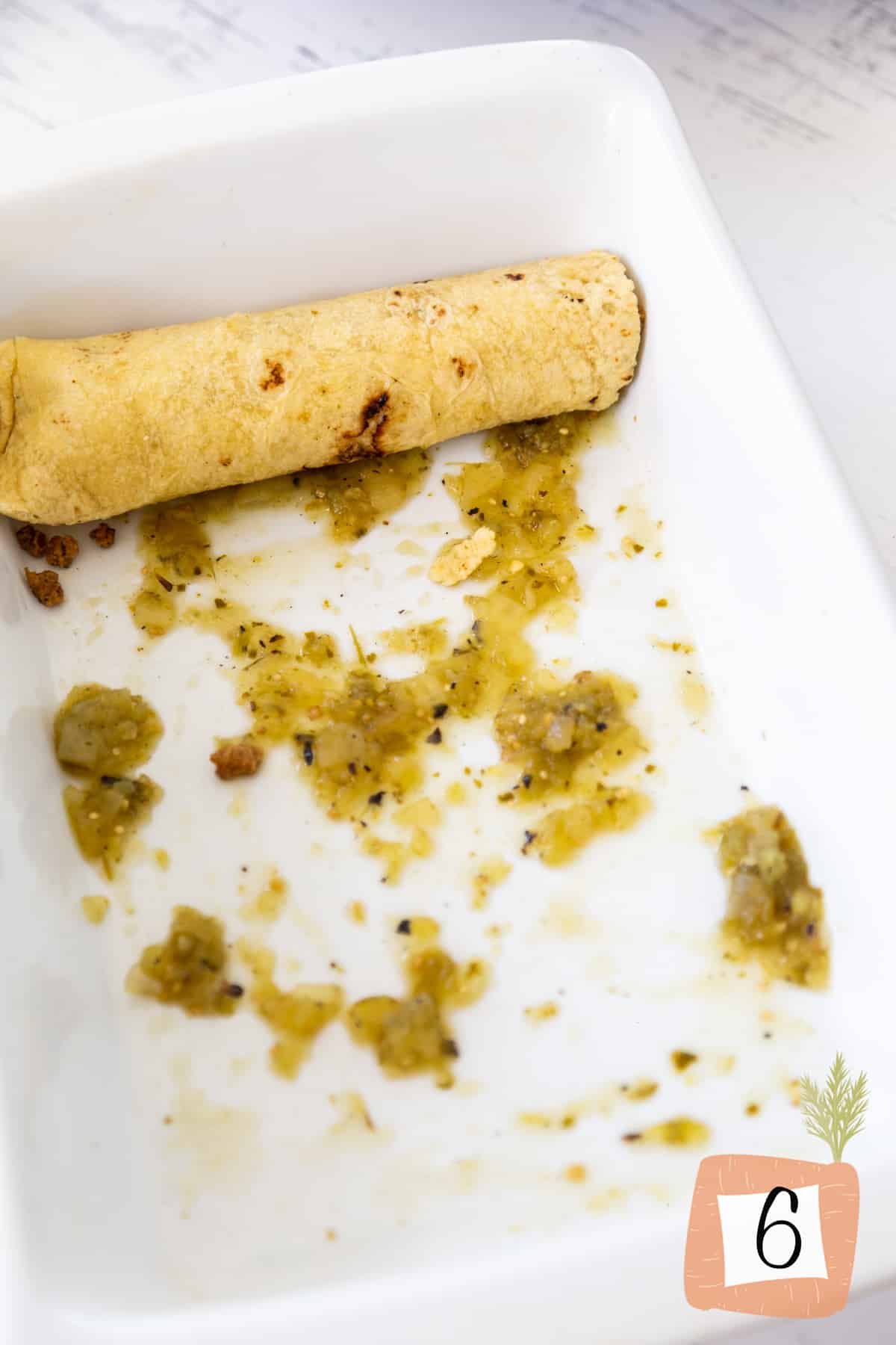 A white baking dish with green salsa and a rolled up corn enchilada.