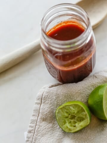 A jar of barbecue sauce with squeezed limes next to it.