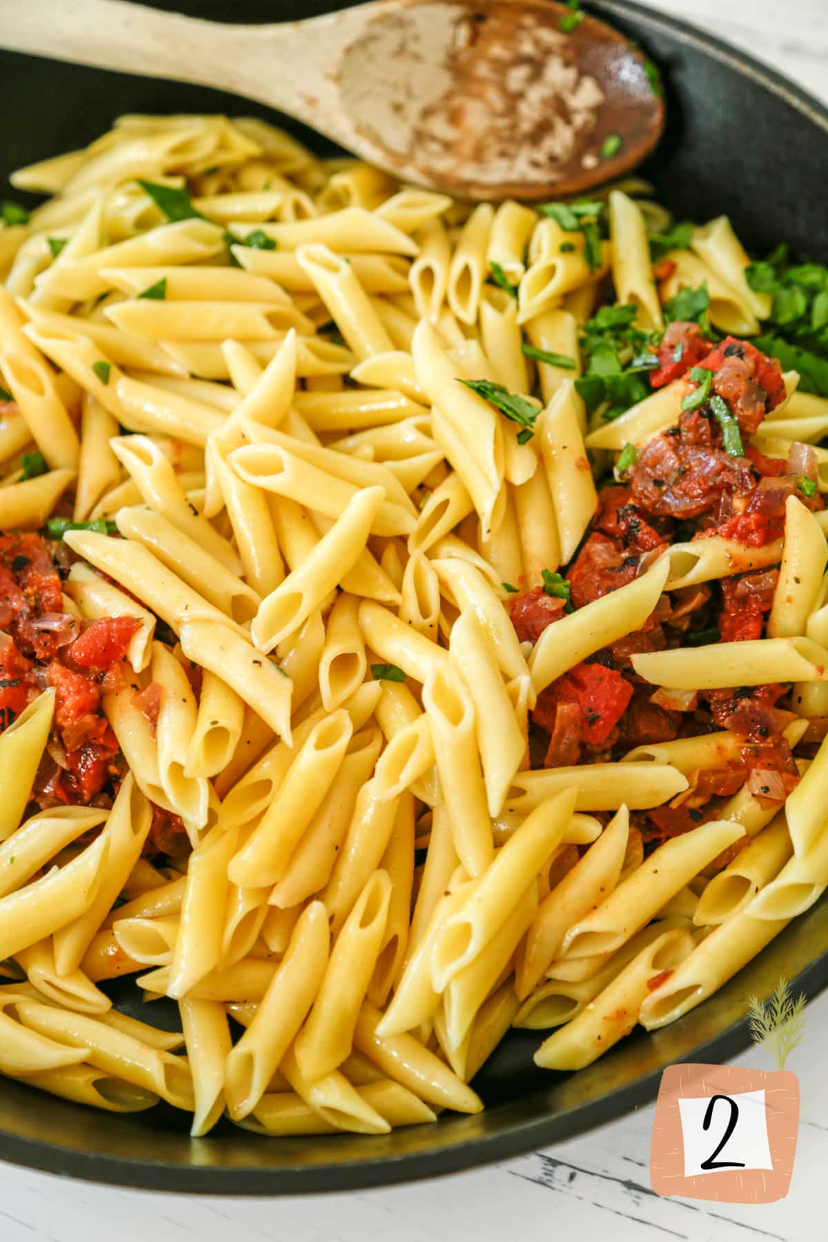 An iron skillet with penne pasta, tomatoes, and spinach.