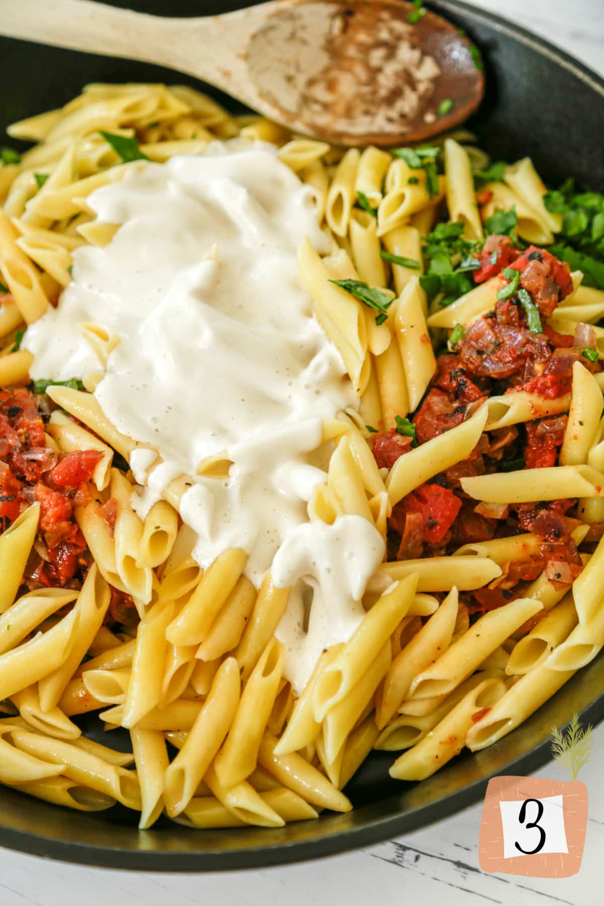 An iron skillet with penne pasta, tomatoes, and a cream sauce.