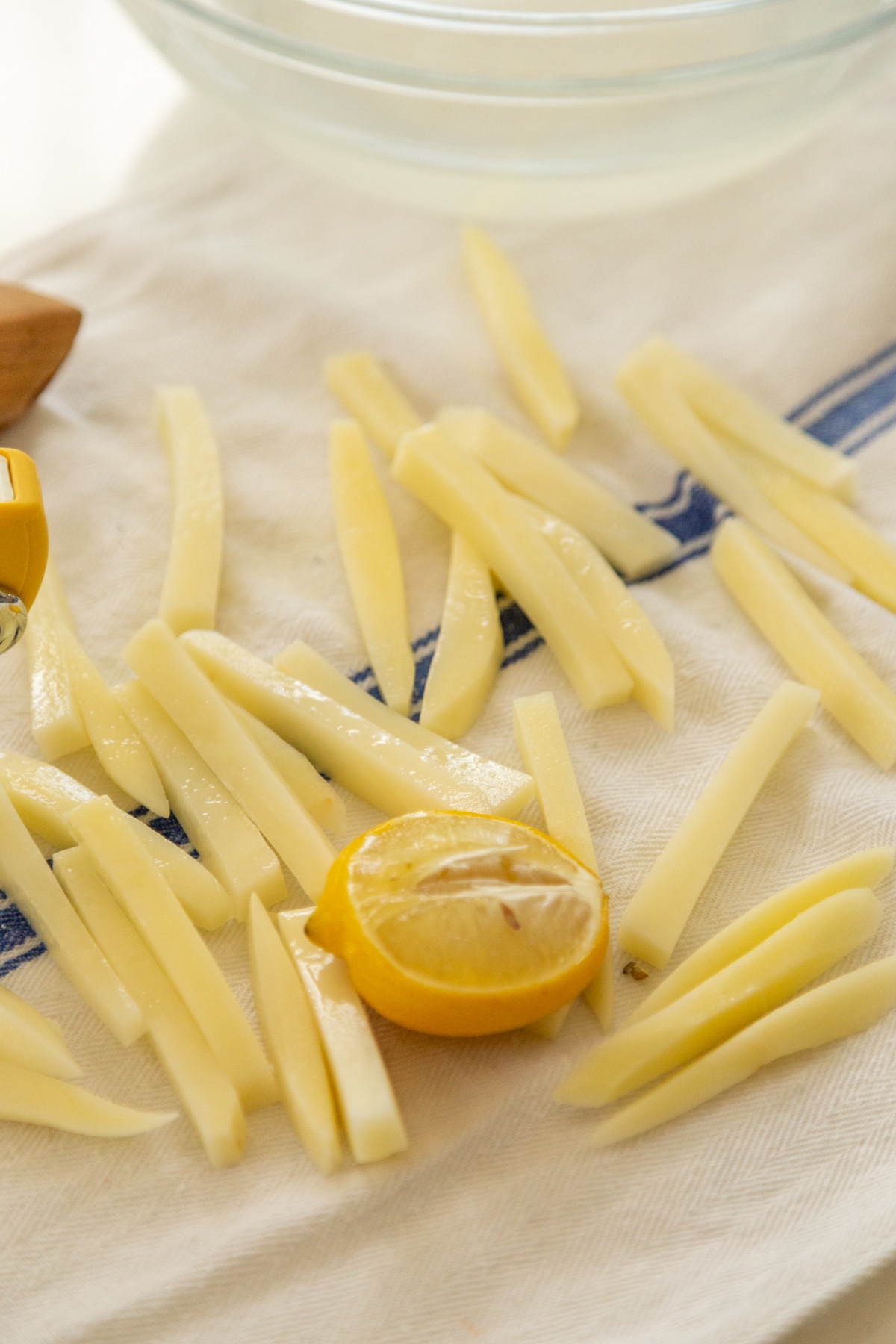 Uncooked french fries and a lemon wedge on a towel.