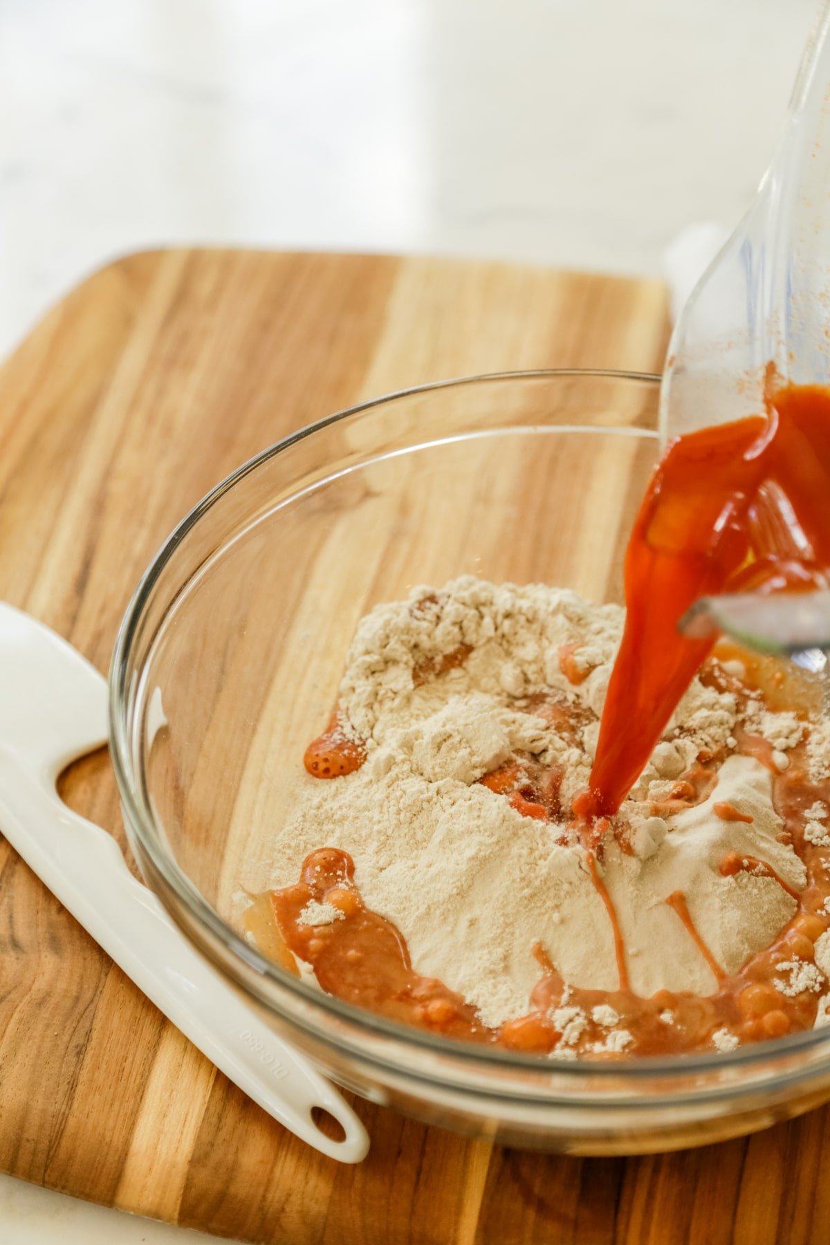 Red liquid being poured into flour in a glass bowl.