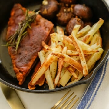 A vegan steak with french fries and mushrooms in a cast iron pan.