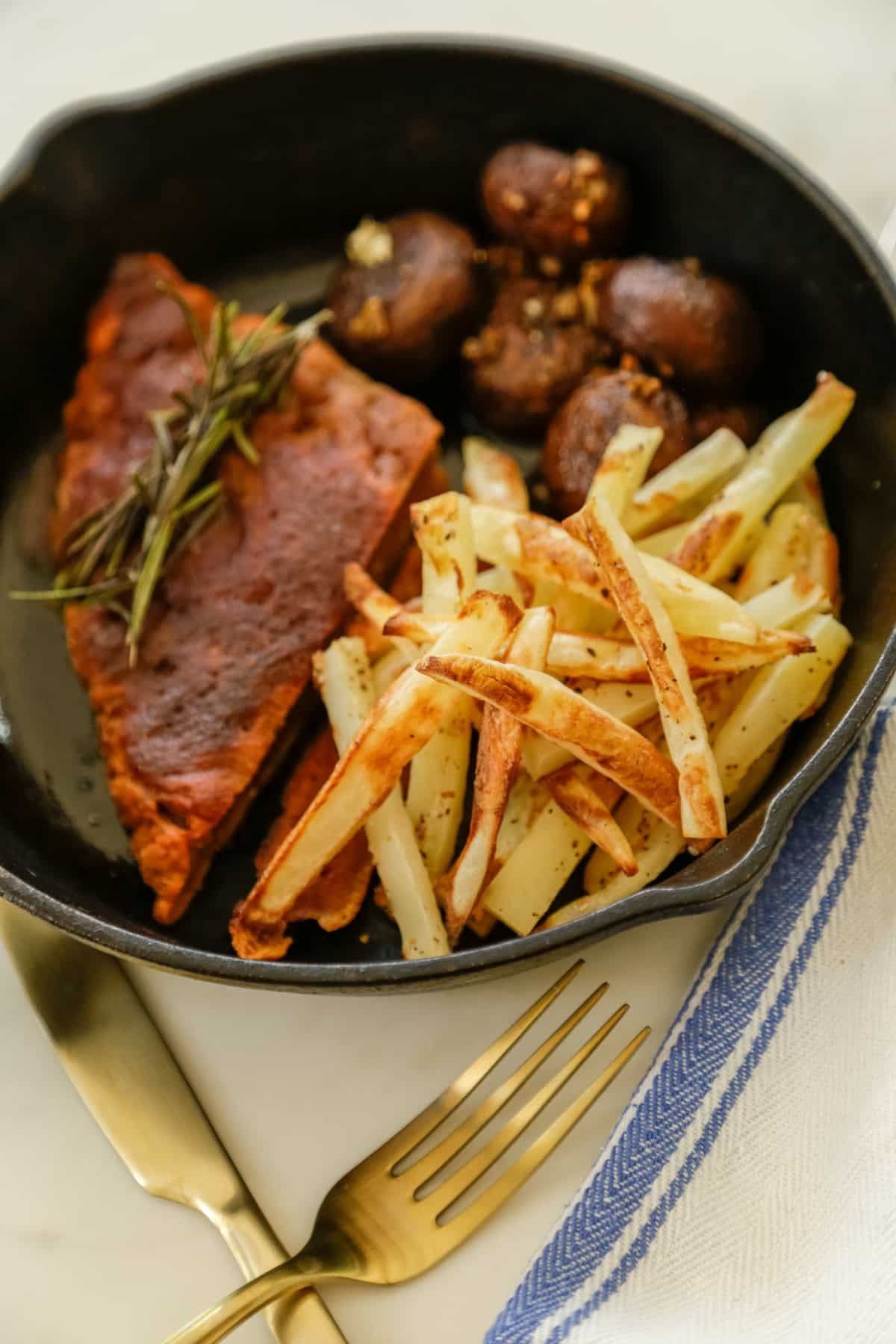 A vegan steak with french fries and mushrooms in a cast iron pan.